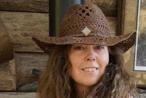 Smiling woman wearing a brown cowboy hat in a rustic wooden cabin setting