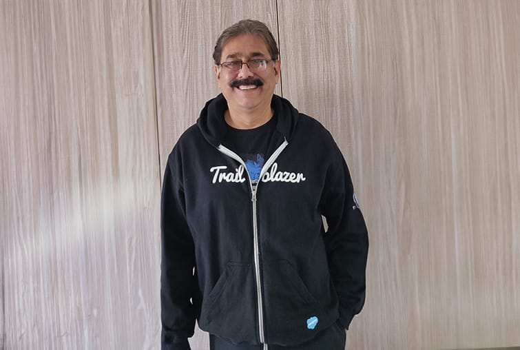 Smiling man with glasses and moustache wearing a black Trailblazer hoodie standing indoors