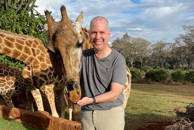Man feeding a giraffe in a wildlife park with other giraffes in the background