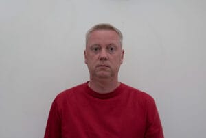 Man in a red shirt standing against a plain white background