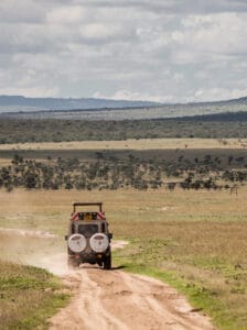 Safari vehicle driving on dirt road in Maasai Mara