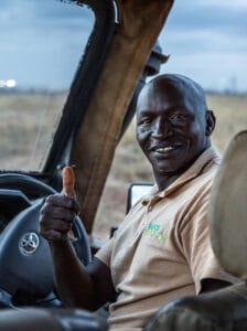 Safari guide at Nairobi Tented Camp smiling and giving thumbs up in 4x4 vehicle