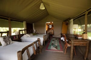 Rustic safari tent with twin wooden beds, desk, and natural decor in the African wilderness