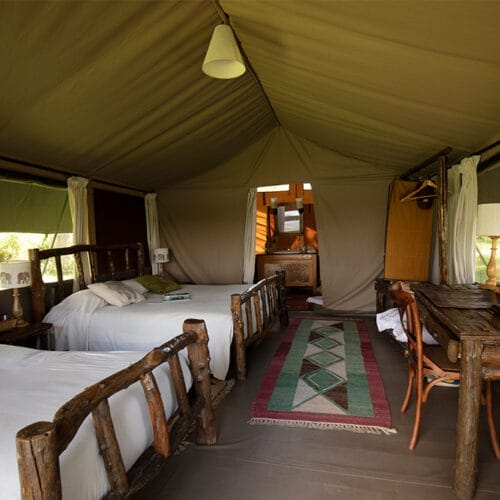 Rustic safari tent with twin wooden beds, desk, and natural decor in the African wilderness