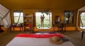 Woman and baby in doorway of safari tent admiring the view at Elephant Peppar Camp in Kenya