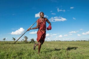 Maasai warrior in traditional attire running across grassy plains in Kenya
