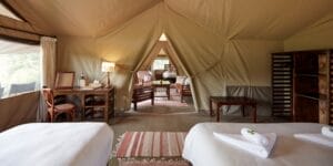 Luxury safari tent interior with twin beds, desk, and lounge area in Kenya