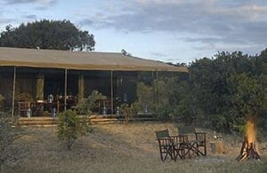 Luxury safari tent with outdoor dining chairs and campfire in the African wilderness
