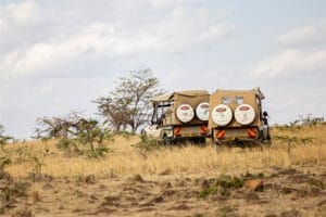 Two safari vehicles from Gamewatchers Safaris driving across dry grasslands in Kenya