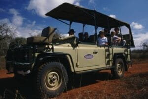 Tourists on African safari in open Land Rover game drive vehicle
