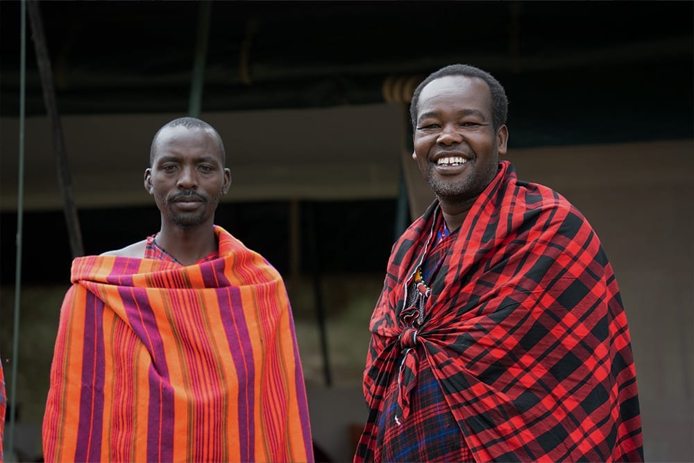 Two Maasai men wearing traditional red and orange shukas smiling outdoors at Porini Giraffe Camp