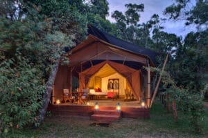 Luxury glamping tent with wooden deck, lanterns, and forest surroundings at dusk