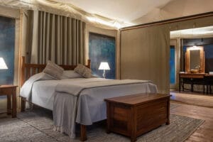 Luxury safari tent bedroom with wooden furniture, soft lighting, and en-suite bathroom