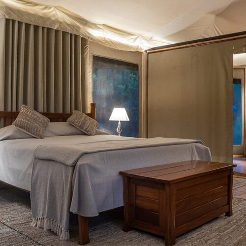 jubileegallery | Gamewatchers Safaris Luxury safari tent bedroom with wooden furniture, soft lighting, and en-suite bathroom