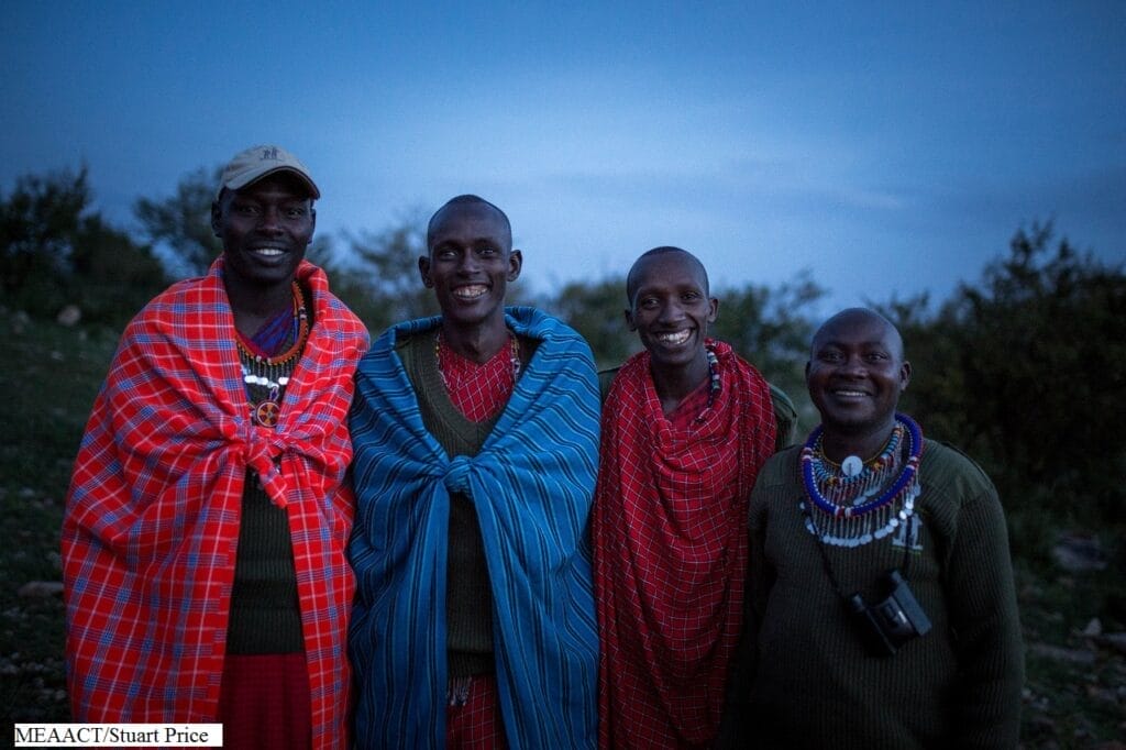 Group of Maasai men in traditional shuka clothing smiling outdoors