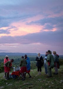 Tourists and Maasai guides enjoying sundowner drinks on safari in Kenya with scenic sunset view
