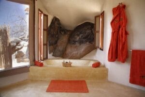 Luxury safari lodge bathroom with stone bathtub, large windows and orange towels in Kenya