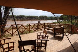 Safari tent deck with wooden chairs overlooking river and acacia trees in Kenya