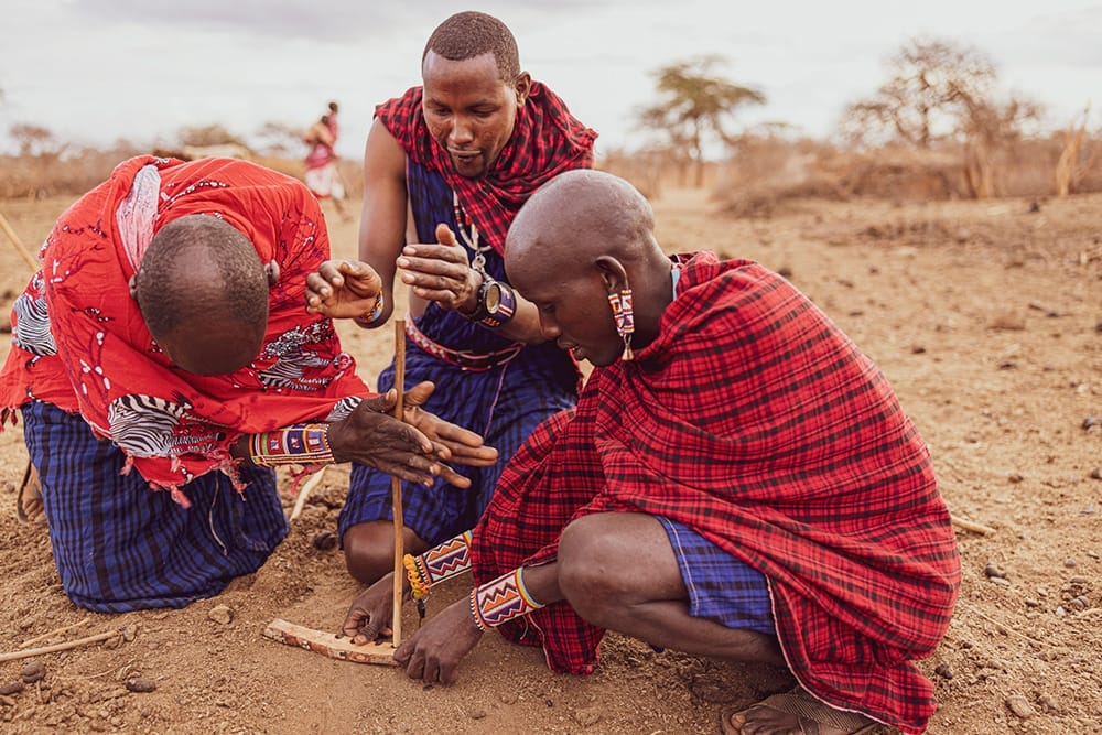 Maasai warriors in traditional attire demonstrating fire-making skills in Kenya