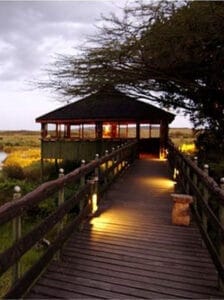 Scenic wooden walkway leading to a safari lodge pavilion at sunset in Kenya