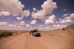 Safari vehicle on a dusty road under a bright blue sky filled with scattered white clouds in a dry open landscape