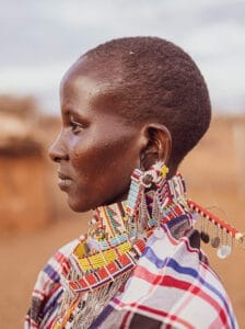 Profile of a person wearing traditional Maasai beadwork jewelry and patterned clothing in a rural setting