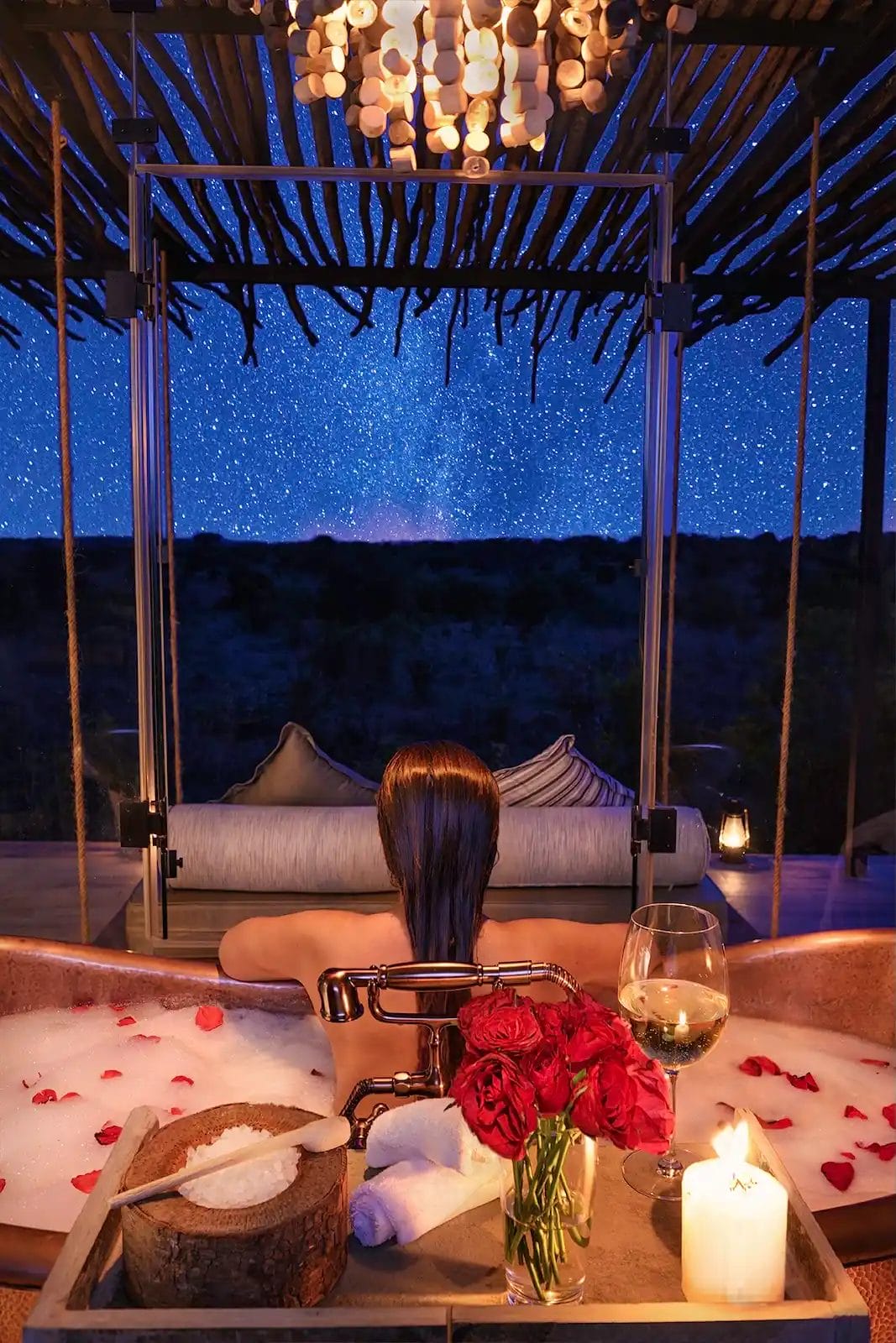 Lady in the bath with petals, looking out onto the night sky at Nimali Mara Camp in the Serengeti, Tanzania