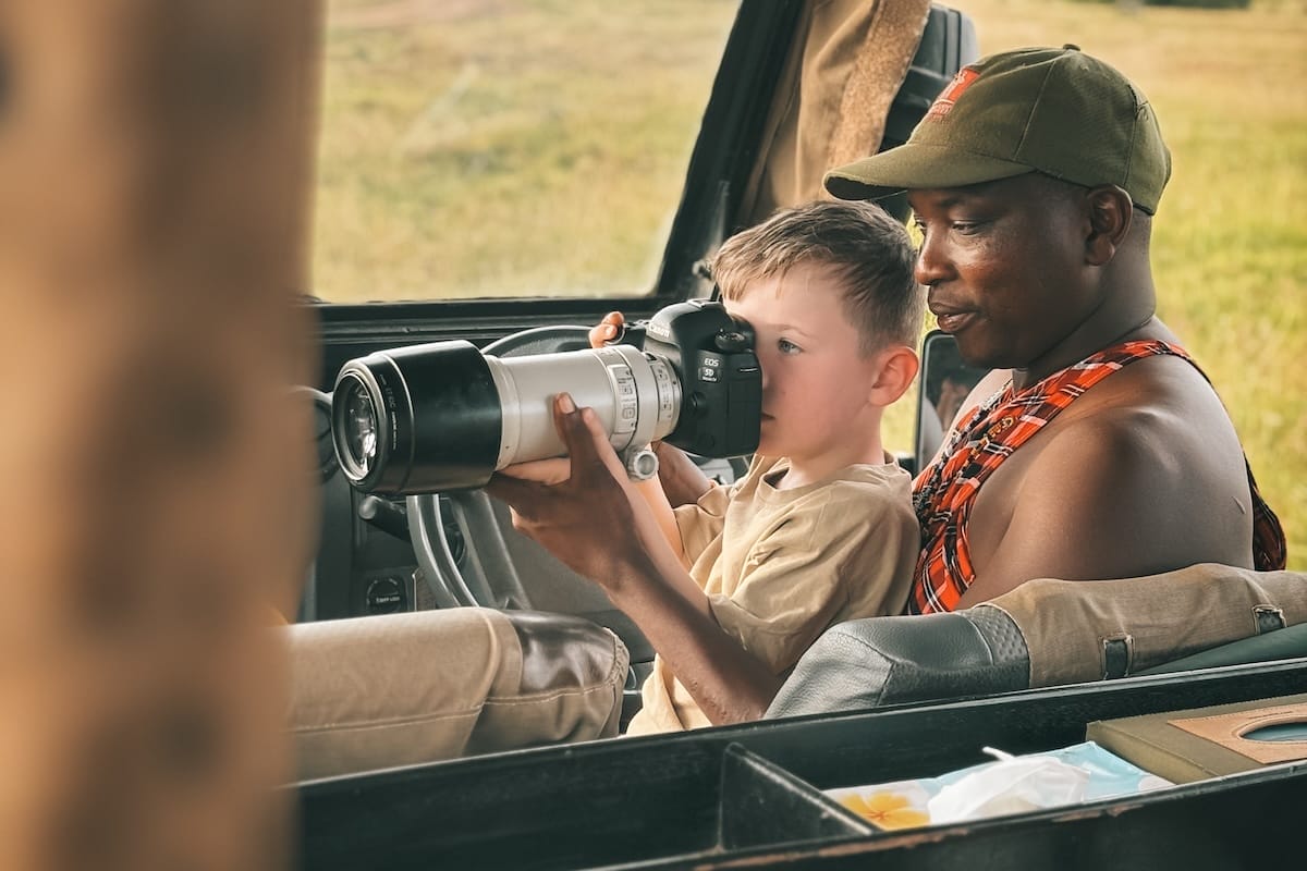 Boy and Guide with Camera sitting in safari vehicle at Ol Kinyei Conservancy photo credit Clare Fisher