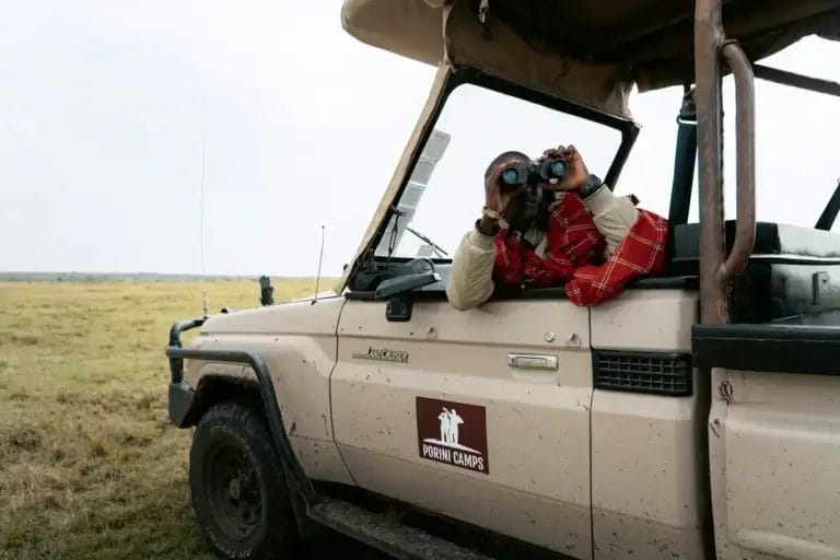 A professional Maasai Guide looks through binoculars at the wildlife scene taken from Porini Lion Camp in Olare Motorogi Conservancy in Kenya. Photo credit Celine & Sacha