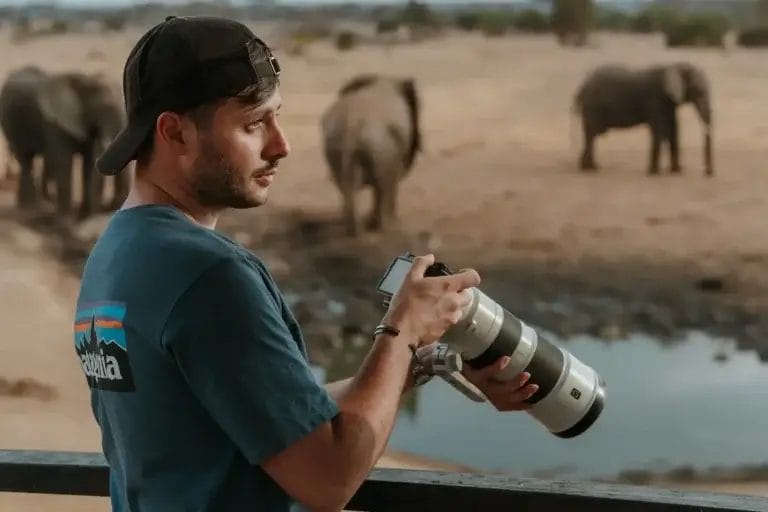 A man holding professional telephoto lens overlooking a classic wildlife photography scene taken from our specialised viewing platform at Porini Amboseli Camp in Selenkay Conservancy in Kenya. Photo credit Celine & Sacha