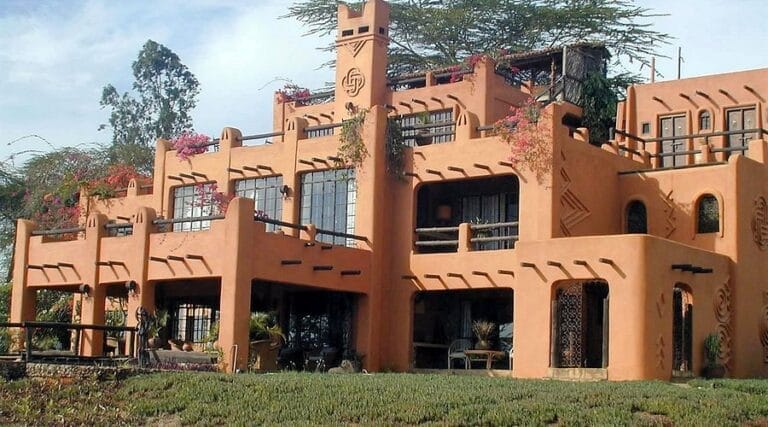 Terracotta adobe-style two-story house with balconies, plants, and decorative geometric patterns on a grassy lawn