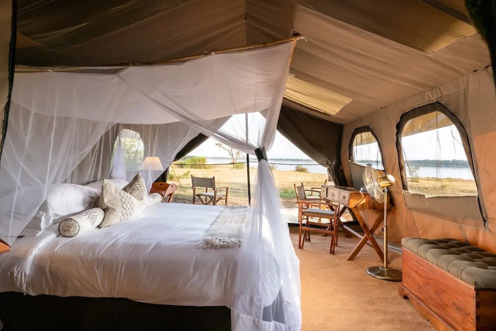 Guest safari tent bedroom with a white canopy bed, sheer curtains, and a lake view at Honey Bear Bush Camp, Uganda.