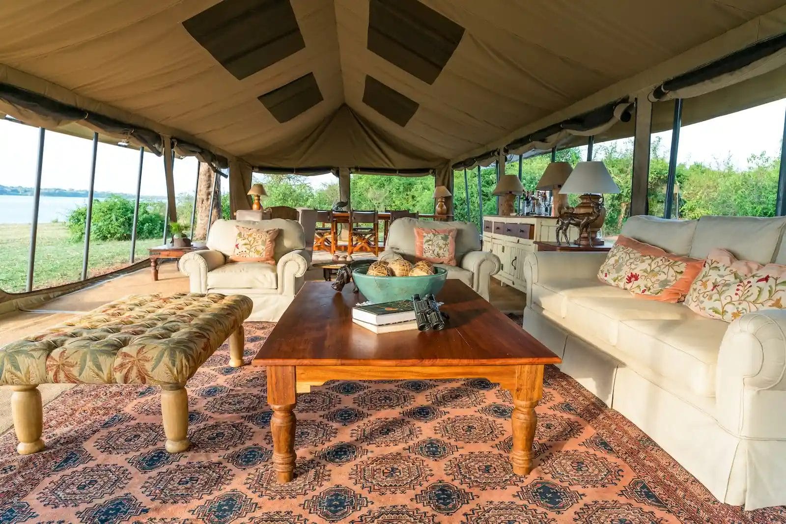 Luxurious tent lounge with cream sofas, floral cushions, a wooden coffee table, and a patterned rug at Honey Bear Bush Camp, Uganda.