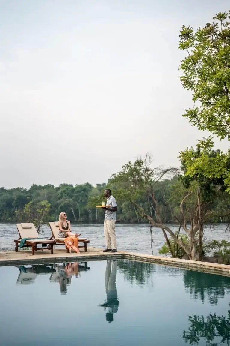 Waiter serves a tray to a woman lounging by a pool at Kulu Ora Lodge In Uganda - photo credit Felix Studios